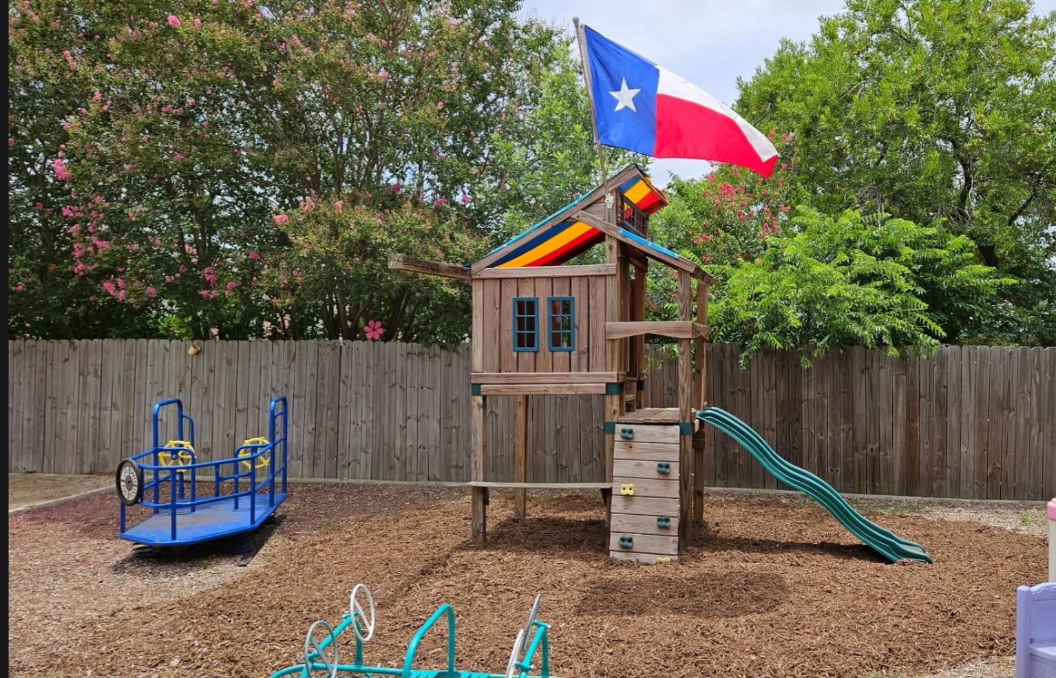 Fenced mulch playground with wooden tower, spinner, and pink playhouse