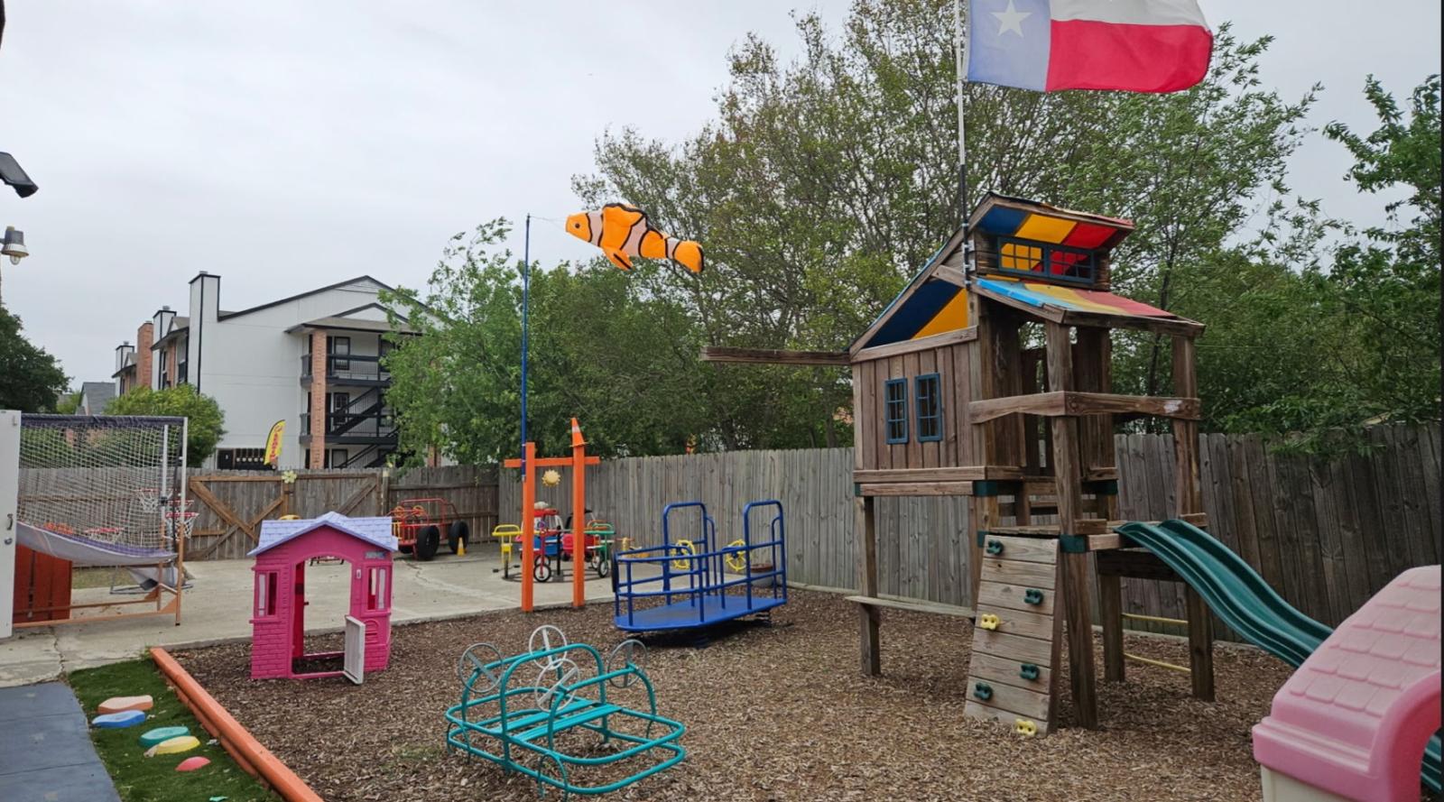 Outdoor play space with basketball hoop, playhouse, spinners, and wooden playset