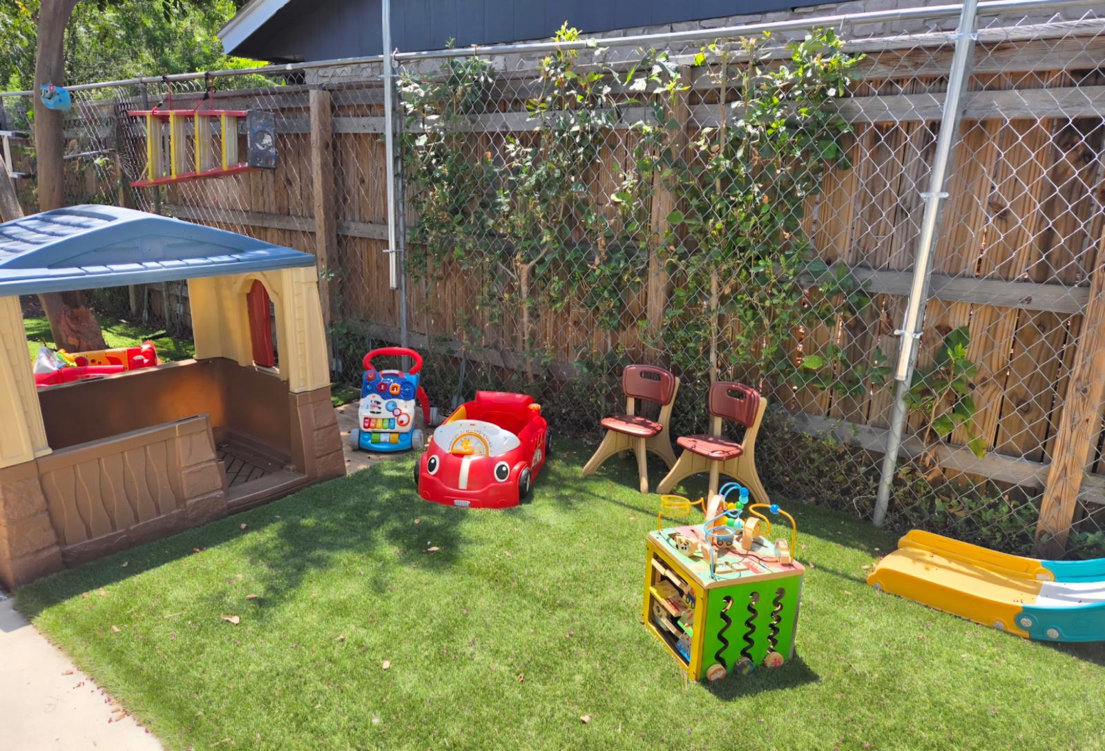Grassy play yard with a cottage playhouse, ride-on car, and toddler activity cube